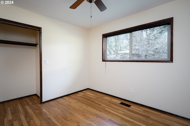 unfurnished bedroom with ceiling fan, a closet, hardwood / wood-style floors, and a textured ceiling