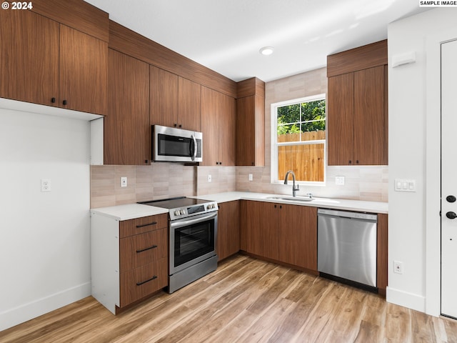 kitchen with light wood-type flooring, stainless steel appliances, tasteful backsplash, and sink