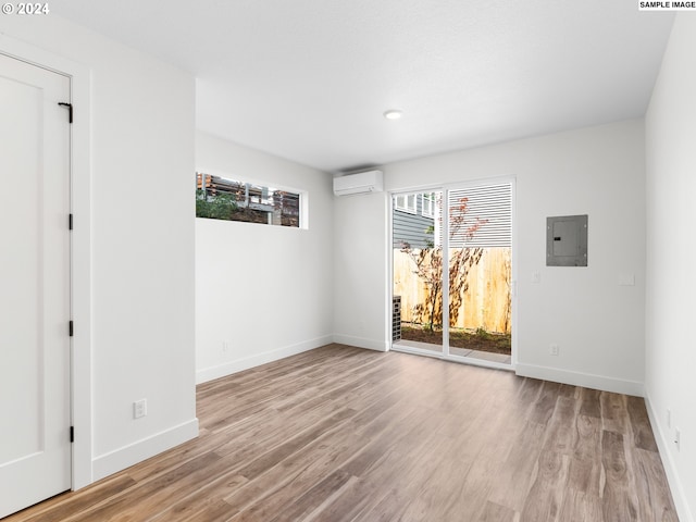 empty room featuring a wall mounted air conditioner, electric panel, and light hardwood / wood-style floors