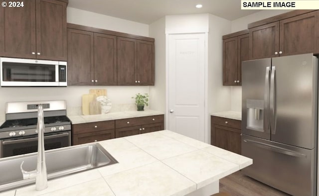 kitchen with sink, tile countertops, dark brown cabinets, hardwood / wood-style flooring, and stainless steel appliances