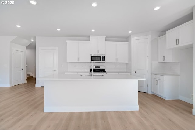 kitchen featuring tasteful backsplash, stainless steel appliances, a center island with sink, and light countertops