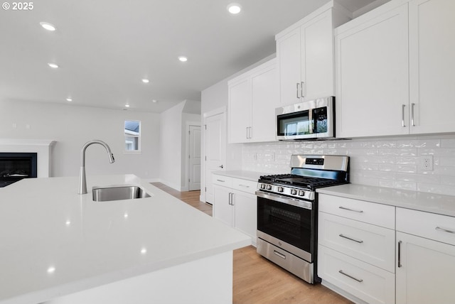kitchen with white cabinets, light countertops, backsplash, a sink, and appliances with stainless steel finishes