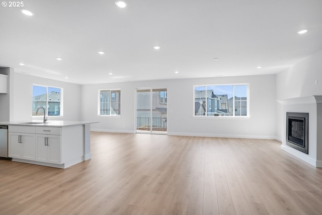 unfurnished living room with baseboards, light wood-style flooring, a glass covered fireplace, and a sink