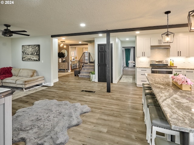 interior space with white cabinetry, a textured ceiling, stainless steel range with electric stovetop, light hardwood / wood-style flooring, and pendant lighting