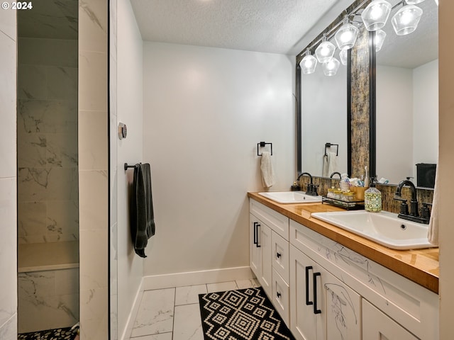 full bathroom featuring marble look tiles, baseboards, double vanity, a textured ceiling, and a shower