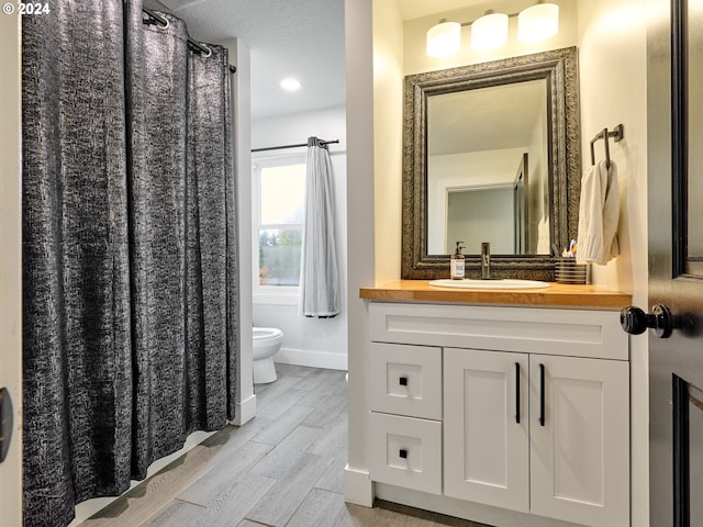 bathroom featuring wood-type flooring, vanity, toilet, and a textured ceiling