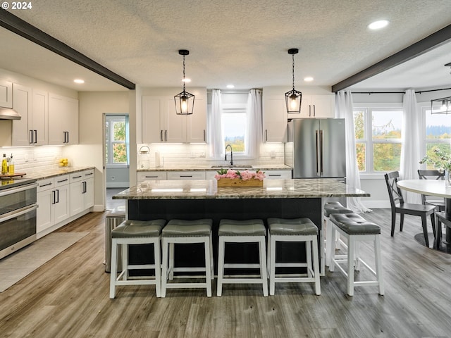 kitchen with stainless steel appliances, beamed ceiling, white cabinetry, and sink