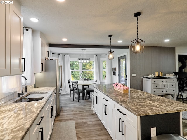 kitchen with light stone counters, a kitchen island, light wood-type flooring, decorative light fixtures, and white cabinets