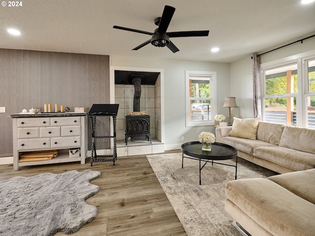 living room featuring light wood-type flooring, a wood stove, ceiling fan, and a textured ceiling