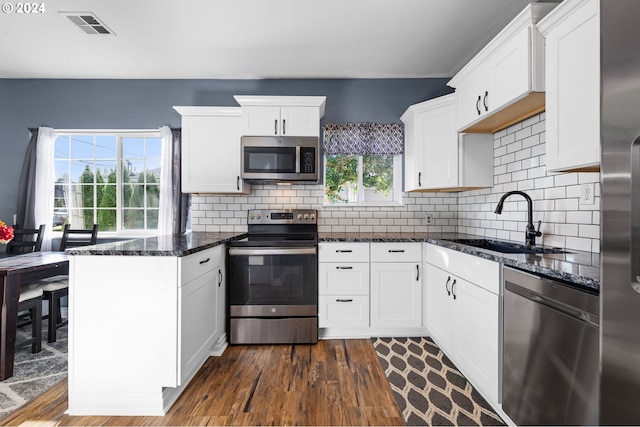 kitchen featuring dark hardwood / wood-style floors, stainless steel appliances, dark stone countertops, sink, and white cabinetry