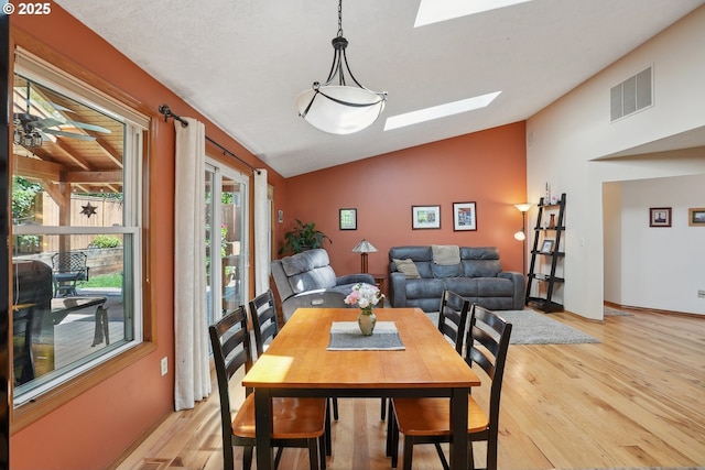 dining space featuring a skylight, vaulted ceiling, and light wood-style floors