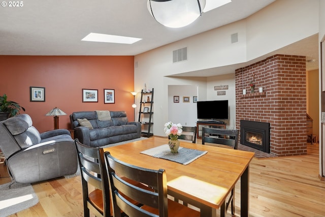 dining space featuring a skylight, light wood-style floors, a fireplace, and high vaulted ceiling