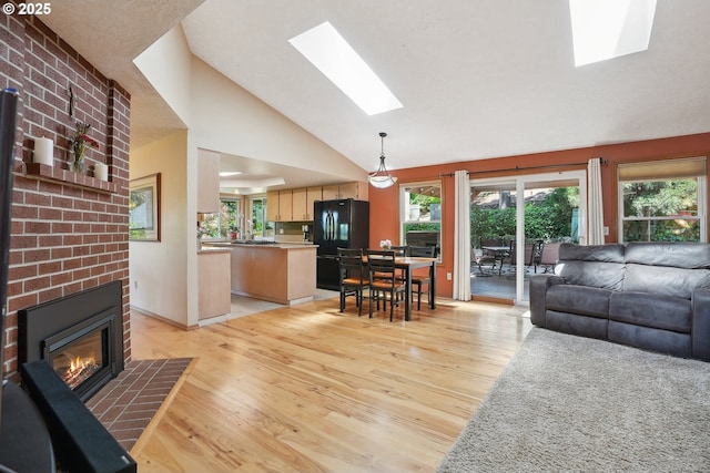 living area with a skylight, light wood finished floors, a fireplace, healthy amount of natural light, and high vaulted ceiling