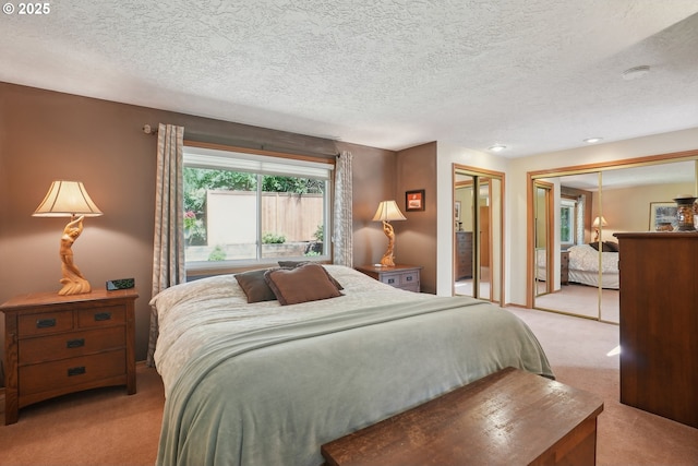 bedroom with light carpet, a textured ceiling, and two closets