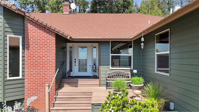 entrance to property with a chimney and a shingled roof