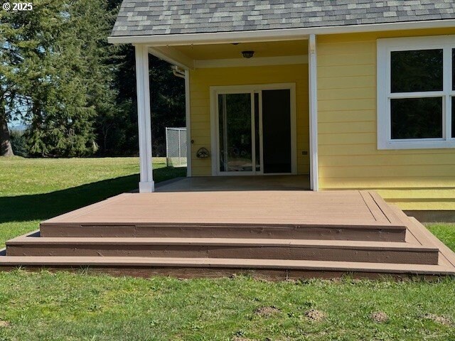 exterior space with a deck, a yard, and a shingled roof