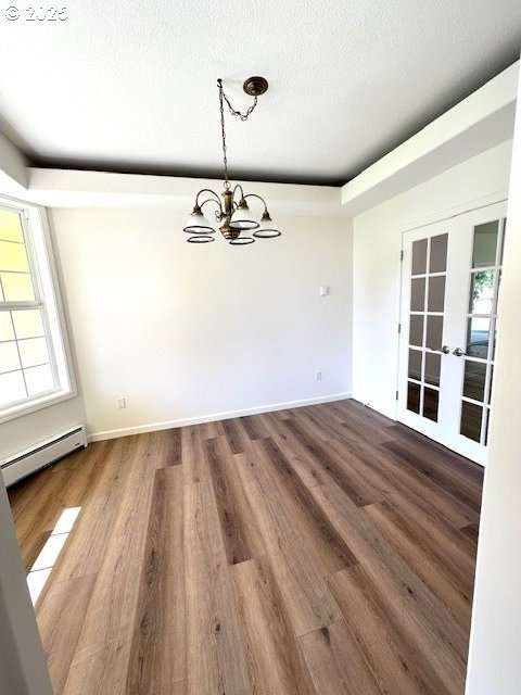 unfurnished dining area with a baseboard heating unit, a chandelier, a textured ceiling, and wood finished floors