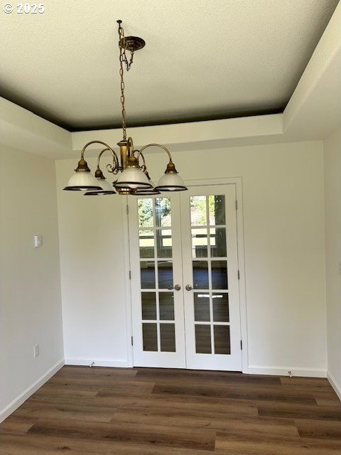 unfurnished dining area with a textured ceiling, a raised ceiling, dark wood finished floors, and baseboards