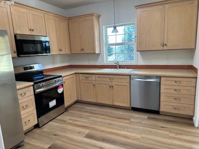 kitchen featuring light wood finished floors, stainless steel appliances, light countertops, light brown cabinets, and a sink