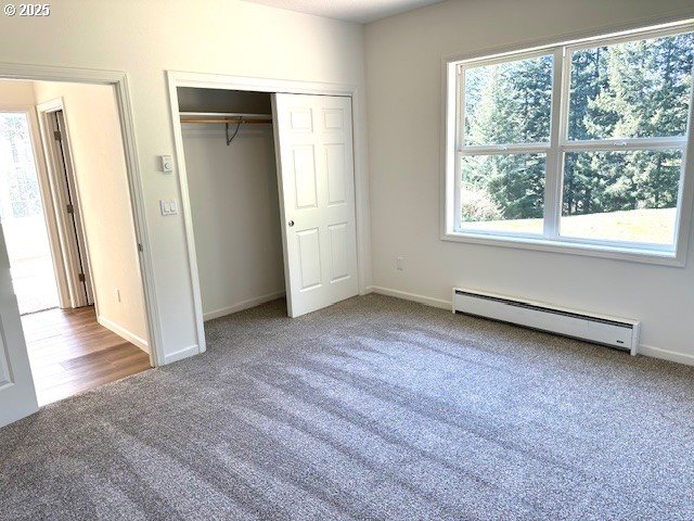 unfurnished bedroom with carpet floors, a closet, baseboards, and baseboard heating