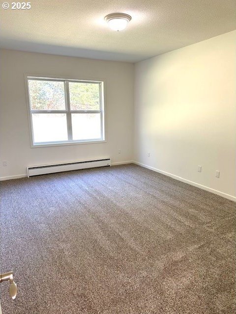 spare room with baseboards, dark carpet, a textured ceiling, and baseboard heating