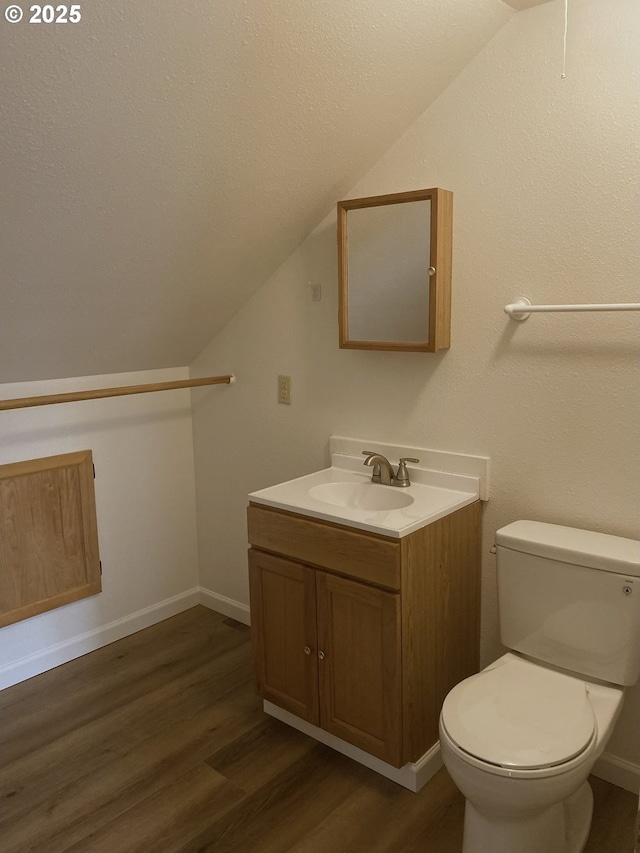 bathroom with lofted ceiling, toilet, wood finished floors, and vanity