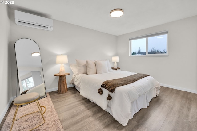 bedroom with wood finished floors, baseboards, and a wall mounted AC