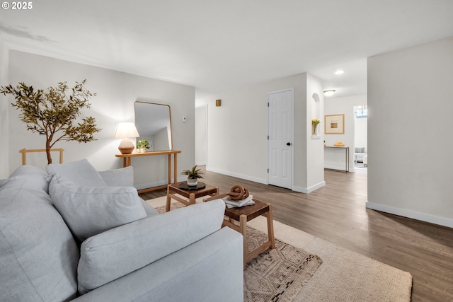 living room featuring arched walkways, recessed lighting, baseboards, and wood finished floors