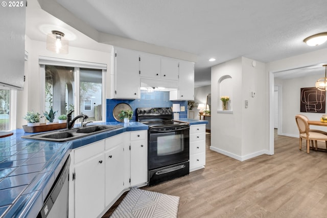 kitchen with a sink, tile counters, black range with electric cooktop, and white cabinetry