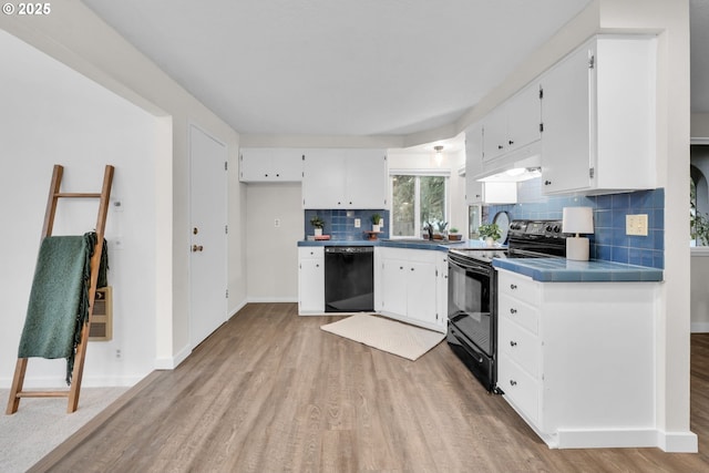 kitchen featuring black appliances, backsplash, tile countertops, light wood-style floors, and white cabinets