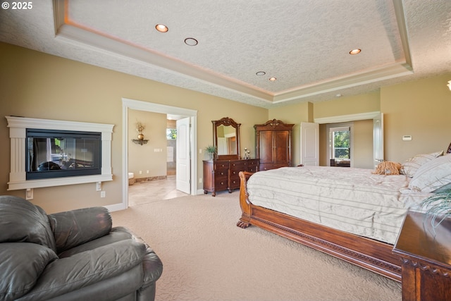 bedroom featuring a textured ceiling, light colored carpet, baseboards, and a raised ceiling