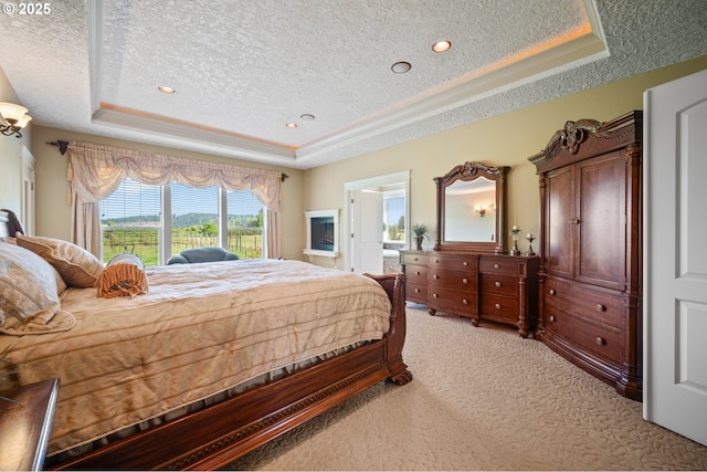 bedroom featuring connected bathroom, a textured ceiling, a tray ceiling, and light carpet