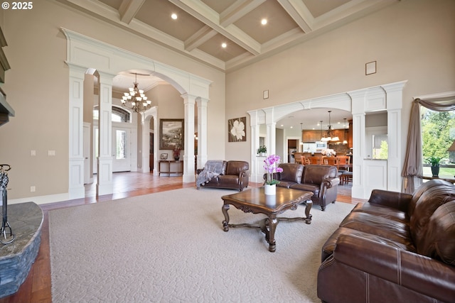 living area with a towering ceiling, beam ceiling, a chandelier, coffered ceiling, and ornate columns