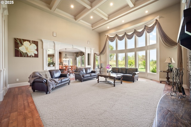 living area featuring a towering ceiling, beamed ceiling, baseboards, ornate columns, and arched walkways