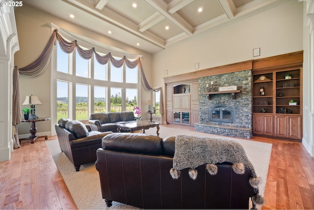 living room featuring light wood finished floors, a stone fireplace, a towering ceiling, beamed ceiling, and coffered ceiling