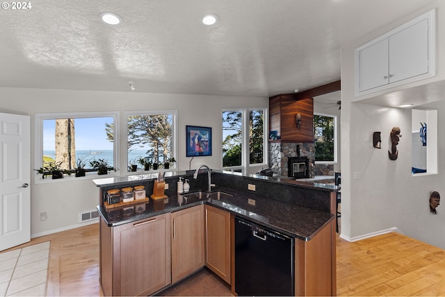 kitchen with sink, a textured ceiling, dark stone counters, black dishwasher, and a healthy amount of sunlight