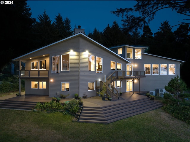 back house at twilight with a balcony, a yard, and a deck