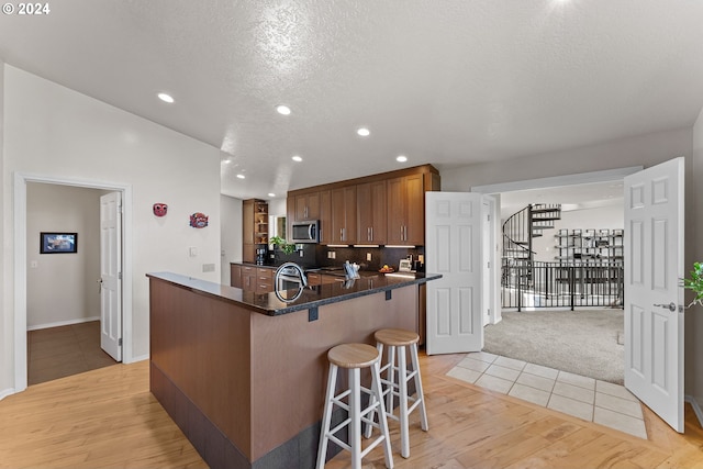 kitchen with sink, light hardwood / wood-style flooring, a center island, a textured ceiling, and a kitchen bar