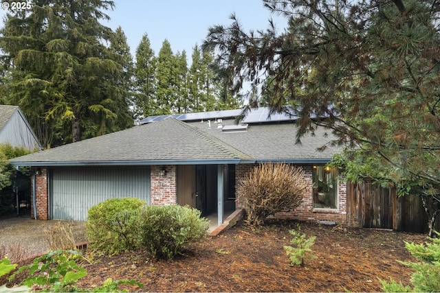 view of front facade with fence, brick siding, roof mounted solar panels, and a shingled roof