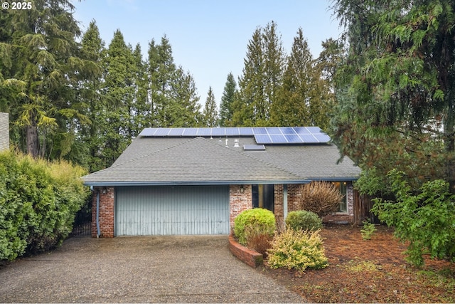 view of front of home featuring brick siding, solar panels, aphalt driveway, roof with shingles, and a garage