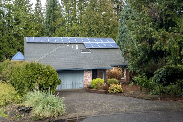 view of front of house with a garage, roof mounted solar panels, roof with shingles, and driveway