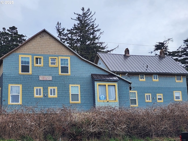 rear view of property with metal roof, a standing seam roof, and a chimney