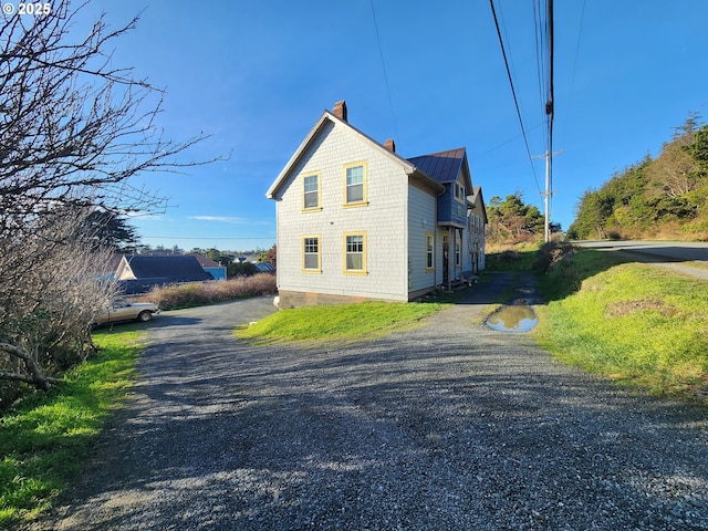 view of side of home featuring gravel driveway, a standing seam roof, a chimney, and metal roof