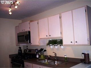 kitchen with a sink, white cabinets, stainless steel microwave, dark countertops, and range with gas cooktop