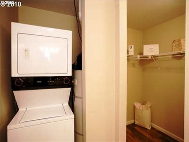 clothes washing area with dark wood-style floors, stacked washer / drying machine, laundry area, and baseboards