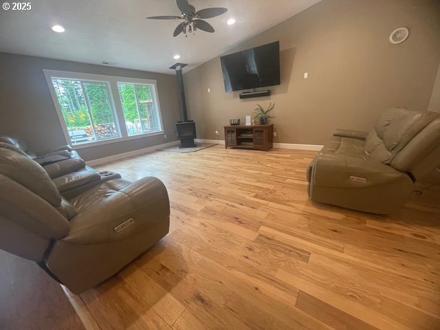 24945 Oak Ln, Elmira, OR 97437 - living room with a wood stove, light wood-style flooring, a ceiling fan, baseboards, and lofted ceiling