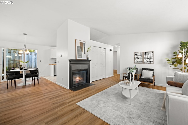 living room featuring a fireplace, light wood finished floors, lofted ceiling, a chandelier, and baseboards