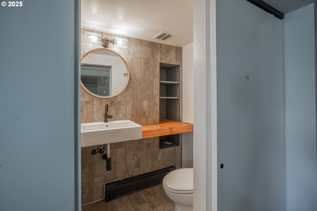 half bath with built in shelves, visible vents, a sink, a baseboard heating unit, and toilet