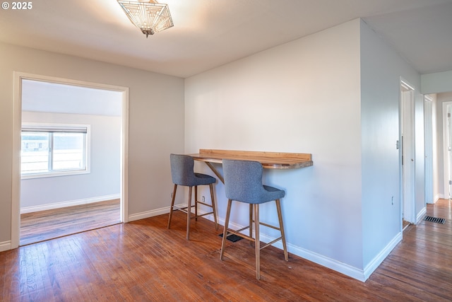 kitchen with visible vents, a kitchen bar, baseboards, and hardwood / wood-style floors