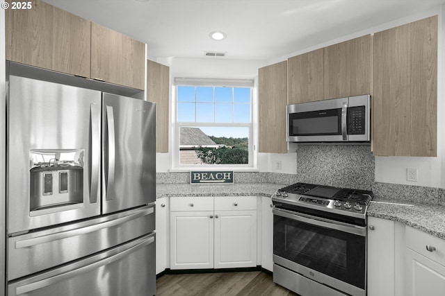 kitchen with light stone counters, white cabinetry, appliances with stainless steel finishes, visible vents, and dark wood-style floors